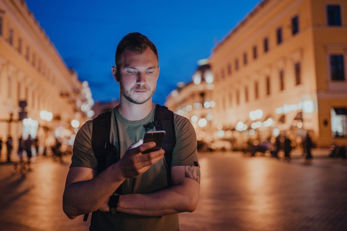 traveler checking a phone at a street corner in the evening, showing how stopping and looking lost increases stress and exposu