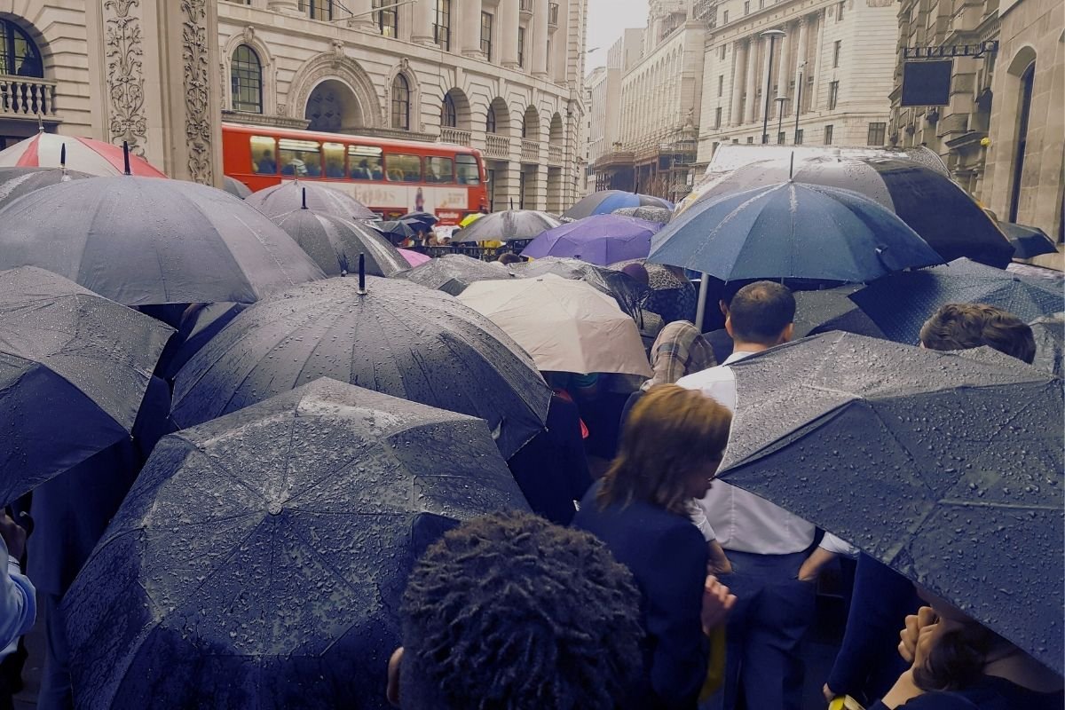 rainy London street with commuters, showing how weather triggers repair spending if your plan has no buffers