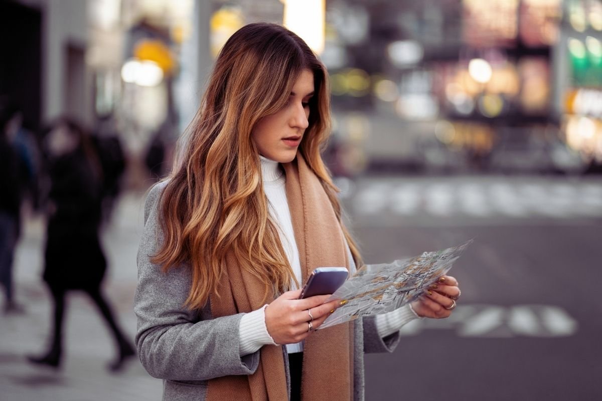 Paris travel mistakes to avoid 2026: traveler looking at a map and phone near a metro entrance, illustrating how choosing the wrong hotel area creates daily transport friction