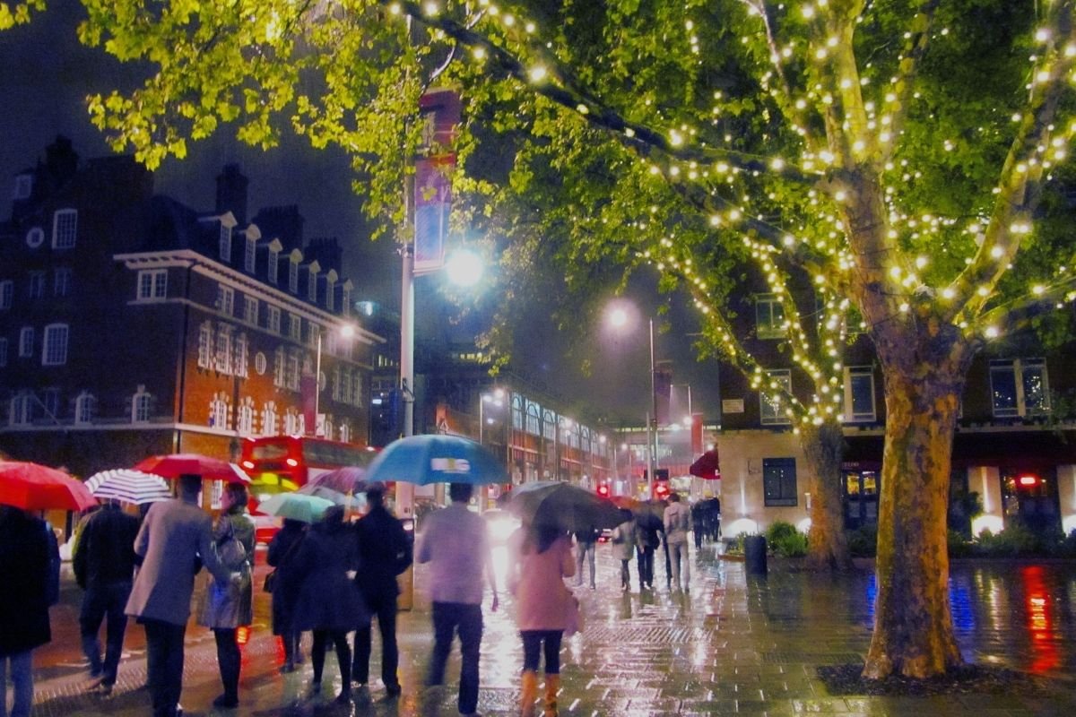 Rainy London street with umbrellas—rain compresses visitors indoors and makes queues heavier, so one anchor plus short loops works best.
