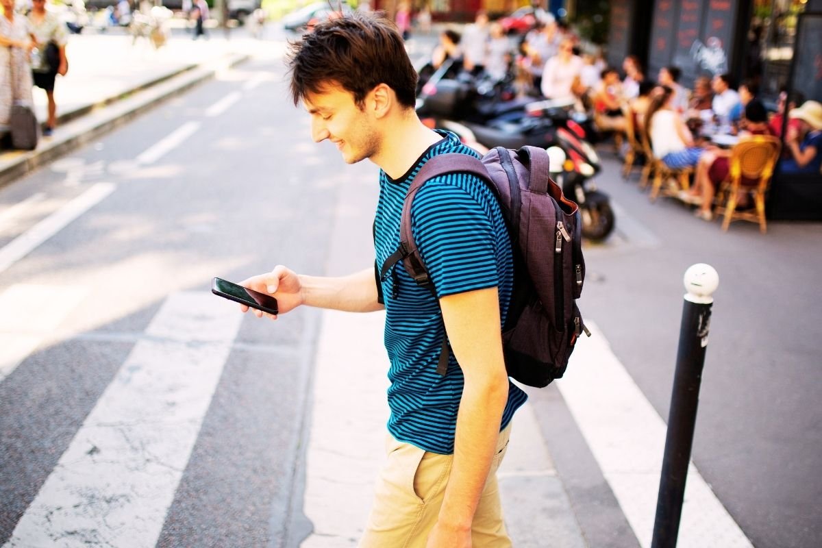 London Safety Guide 2026: tourist holding phone near a busy crossing, showing a common vulnerable posture for phone snatching