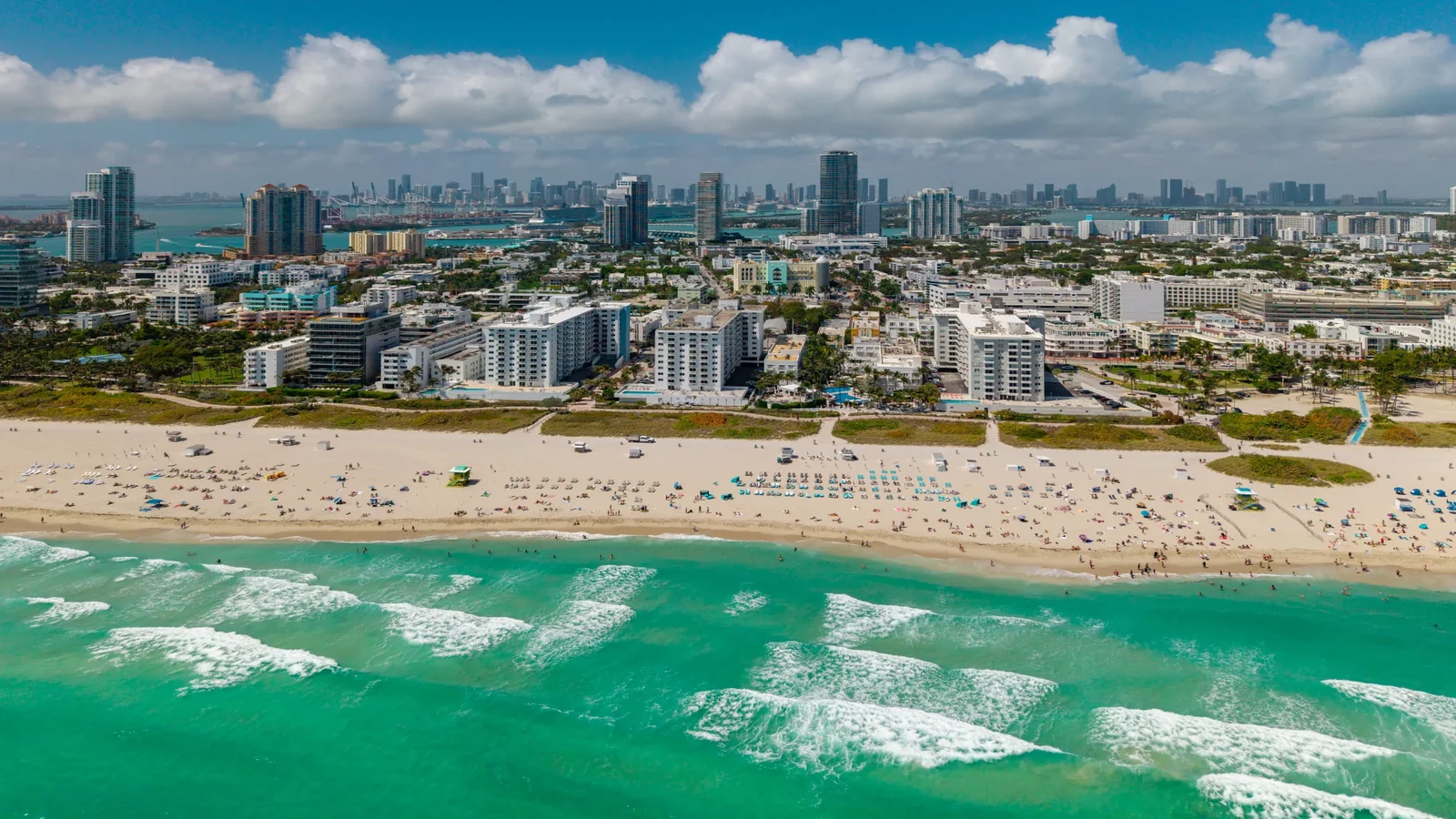 Aerial view of Miami Beach shoreline with turquoise Atlantic Ocean waters and the Miami skyline in the background.