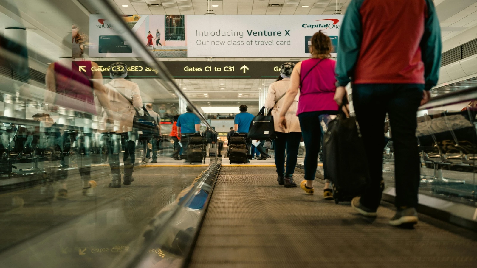 Travelers with luggage walking through a busy airport terminal.