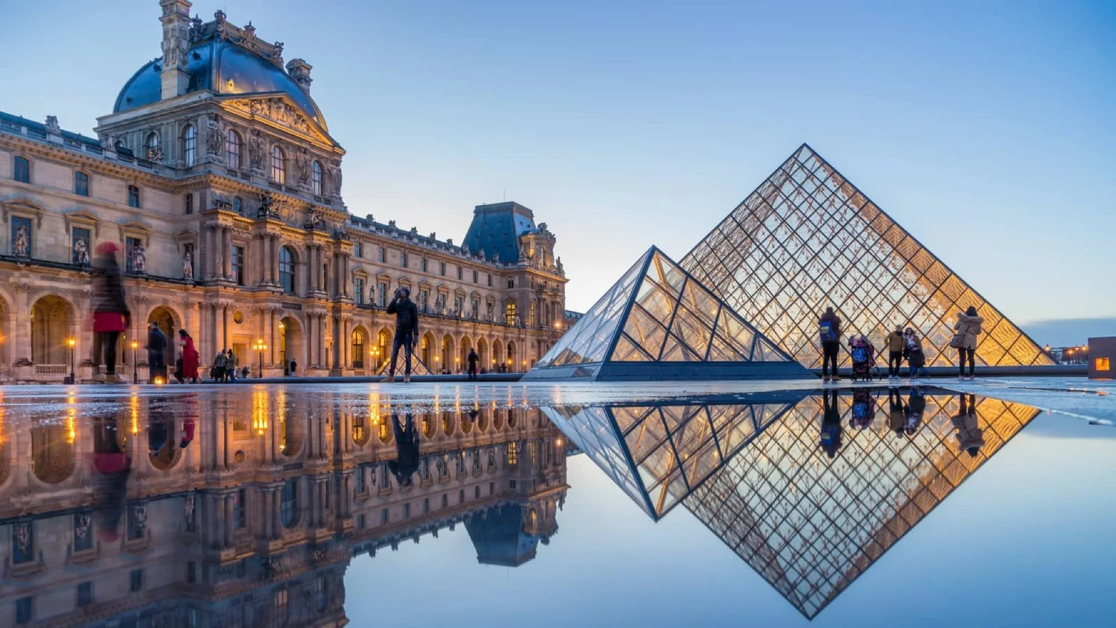 The Louvre Pyramid at sunset reflecting in the water outside the Louvre Museum in Paris.