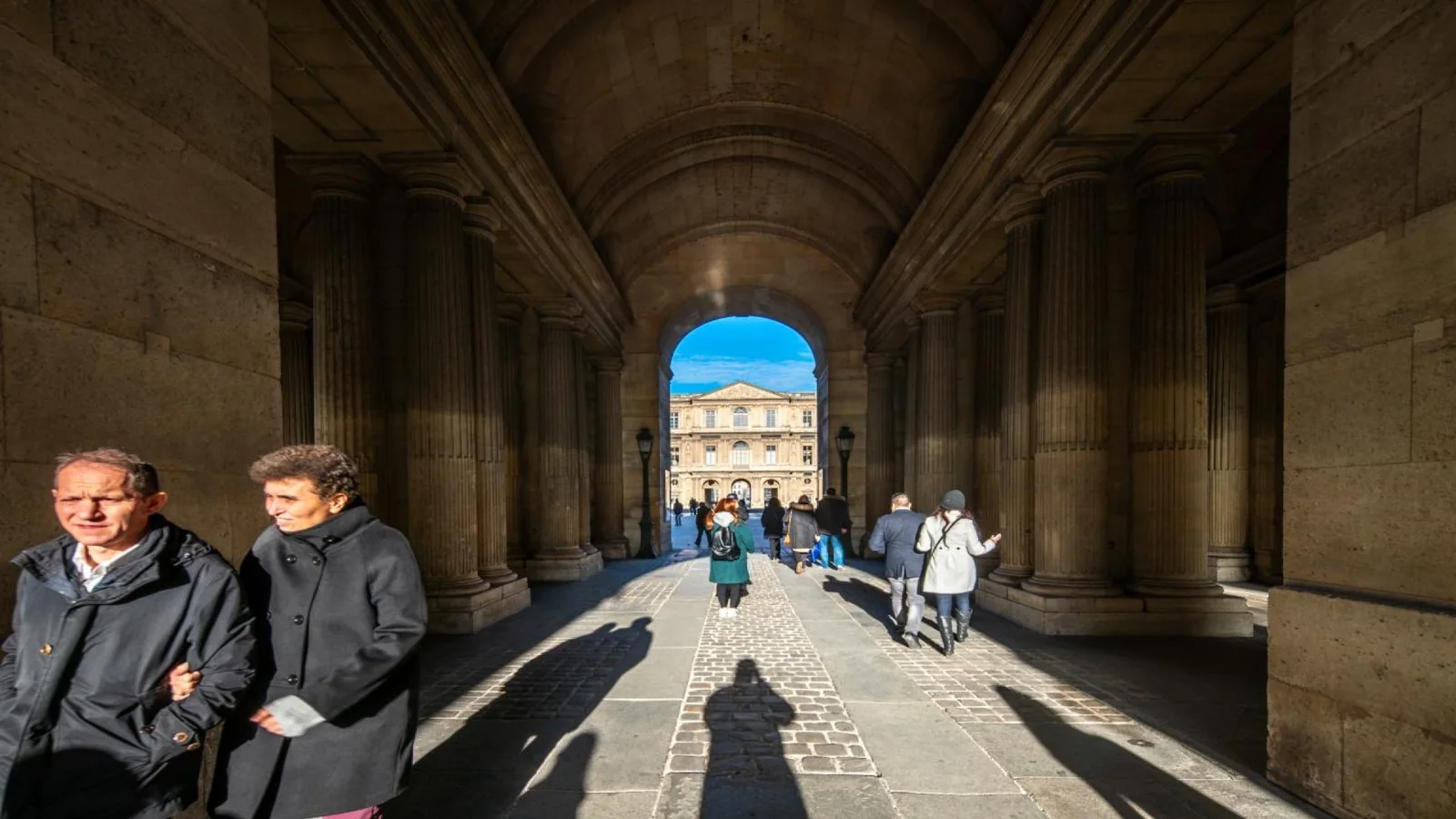Visitors walking through a historic arcade toward the museum in Paris.
