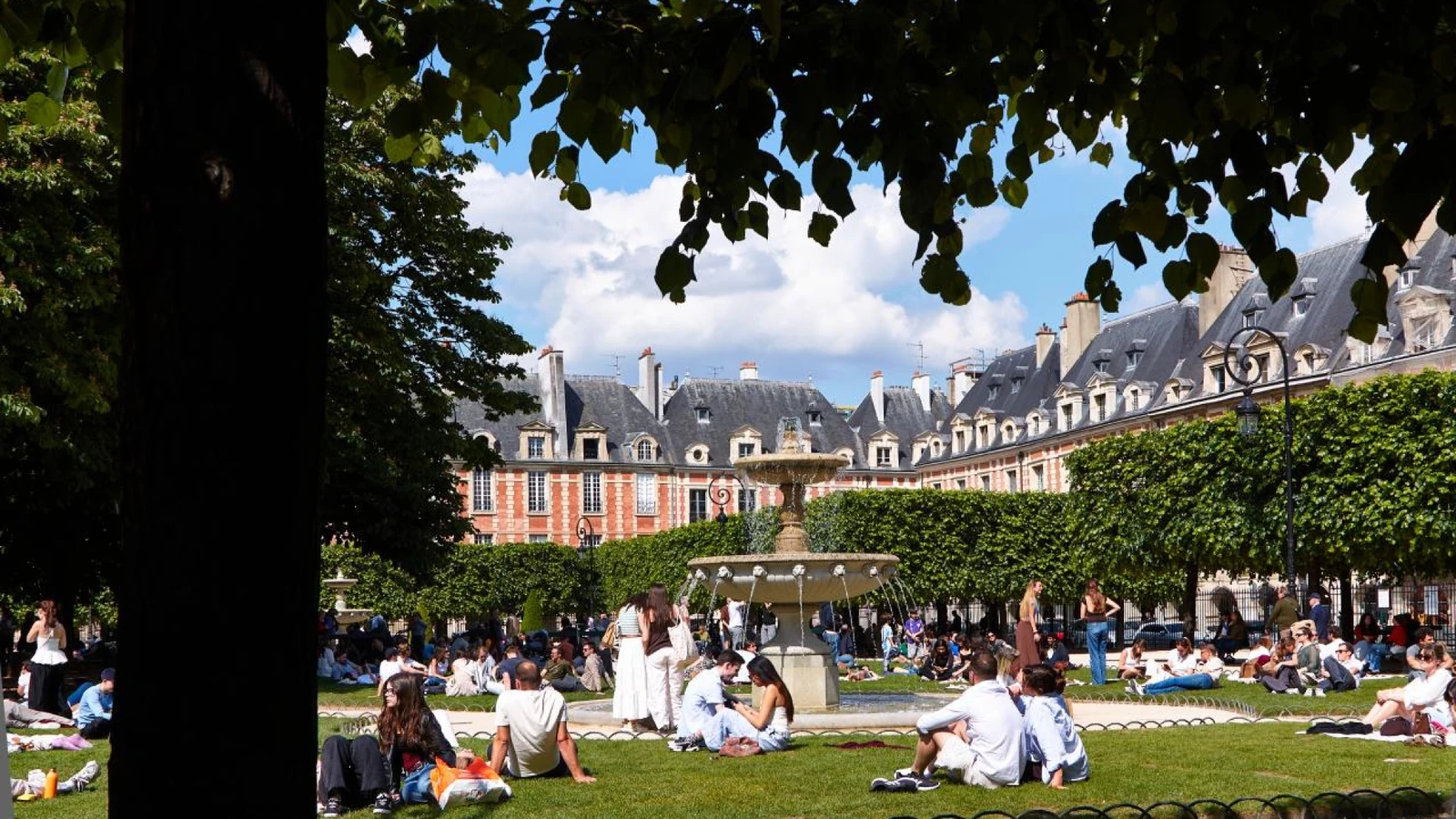 Visitors relaxing on the lawn around the fountain in a historic Paris square