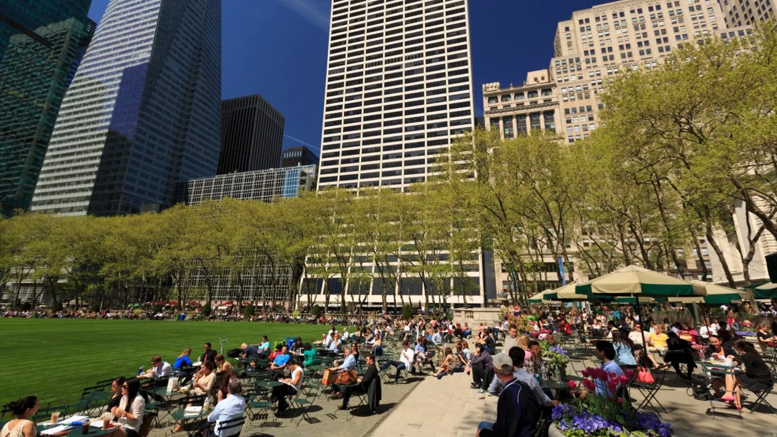 Visitors relaxing in Bryant Park beneath Midtown Manhattan skyscrapers in New York