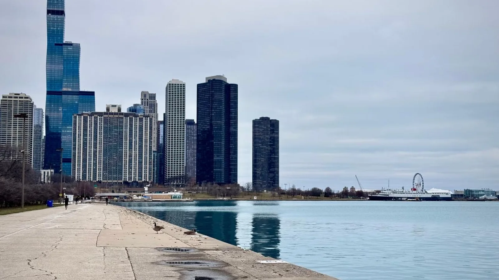 Chicago skyline beside Lake Michigan under an overcast sky, viewed from a waterfront path.