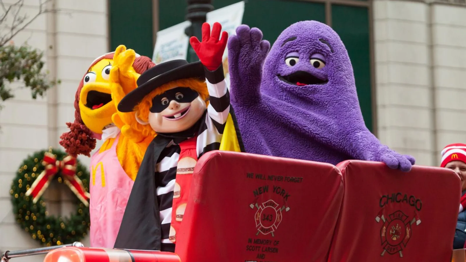 Colorful costumed characters waving from a decorated parade vehicle.