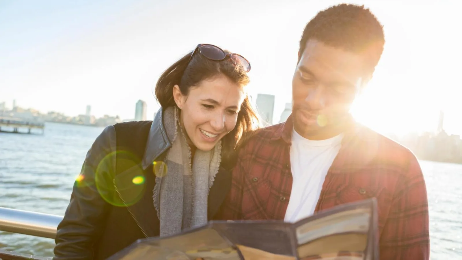Couple reading a paper city map beside the water in warm sunlight