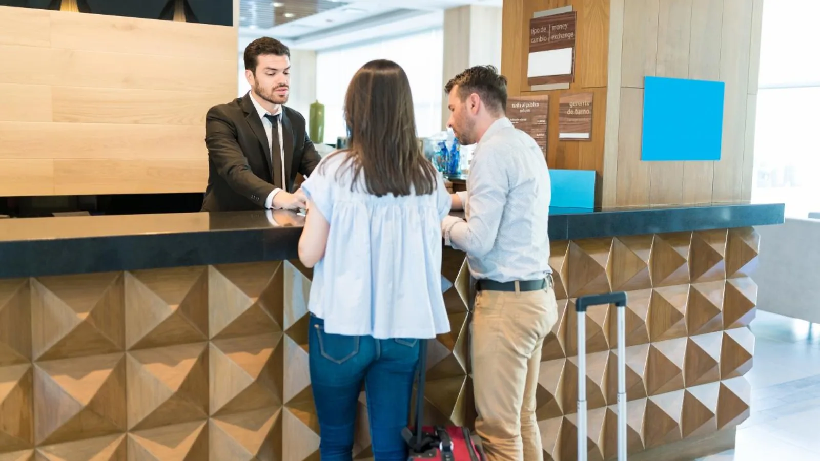 Couple with luggage checking in with a receptionist at a hotel reception desk