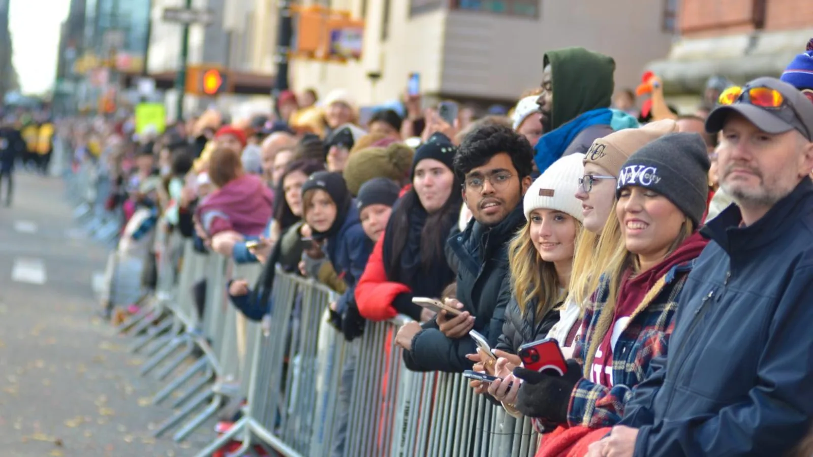 Spectators behind barriers along a crowded New York City Thanksgiving parade route