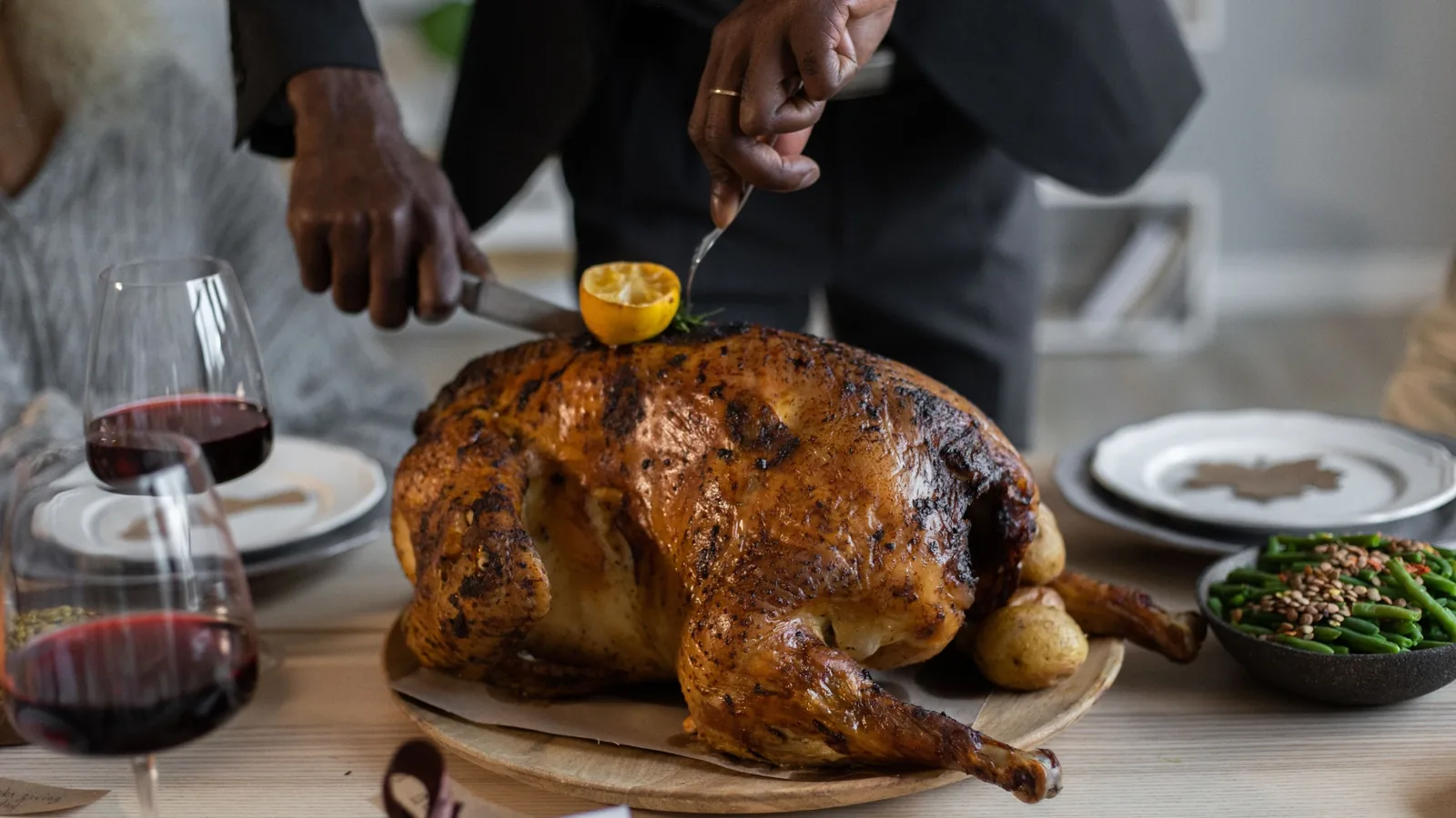 Roast turkey being carved at a Thanksgiving dinner table with side dishes and wine glasses